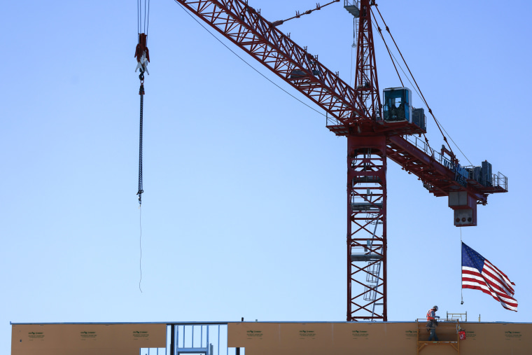 An American flag flies from a crane near a construction worker during the construction of a new building.